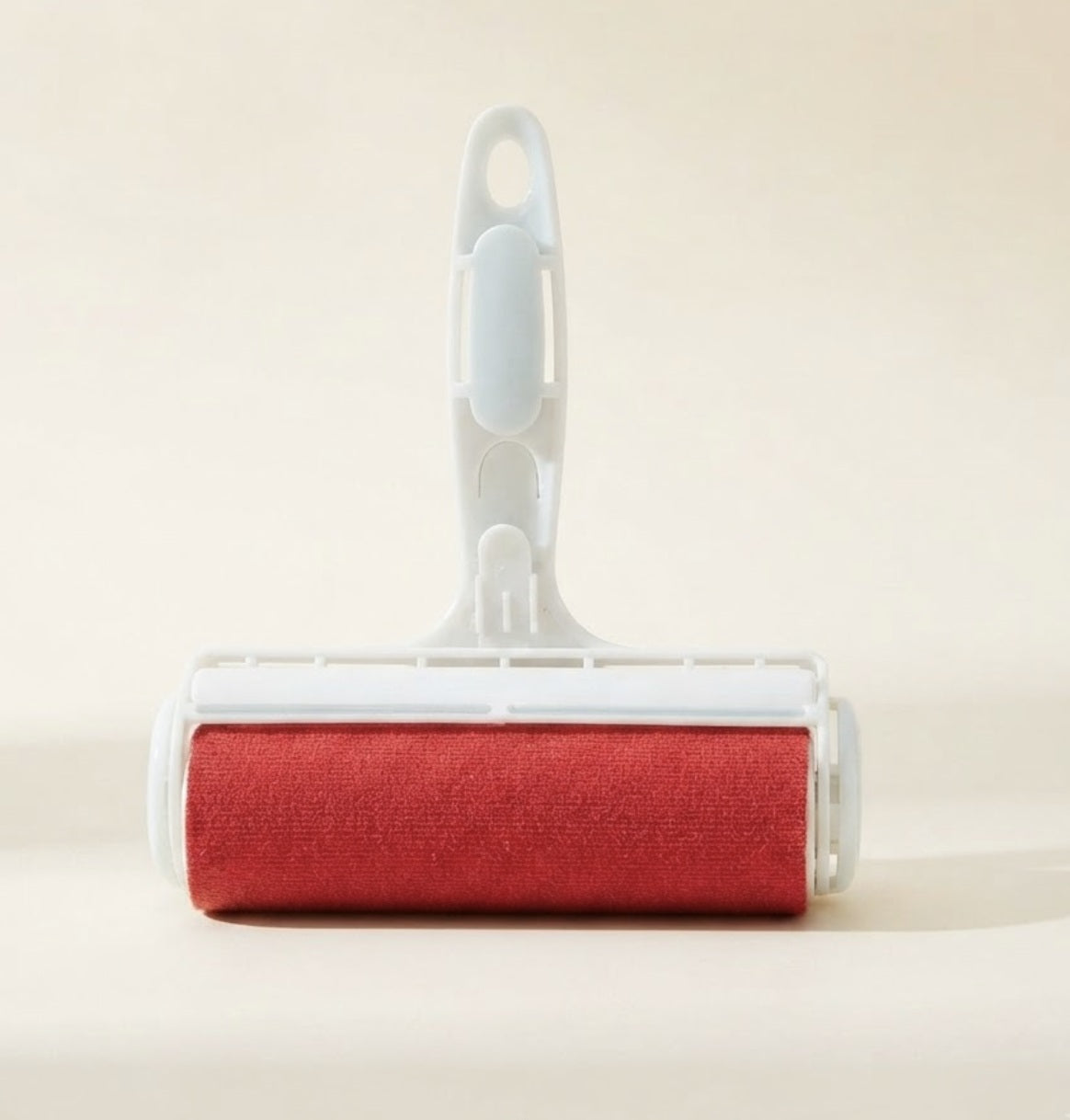 Rodillo quita pelos reutilizable para mascotas, cuerpo blanco con rodillo rojo, sobre fondo crema